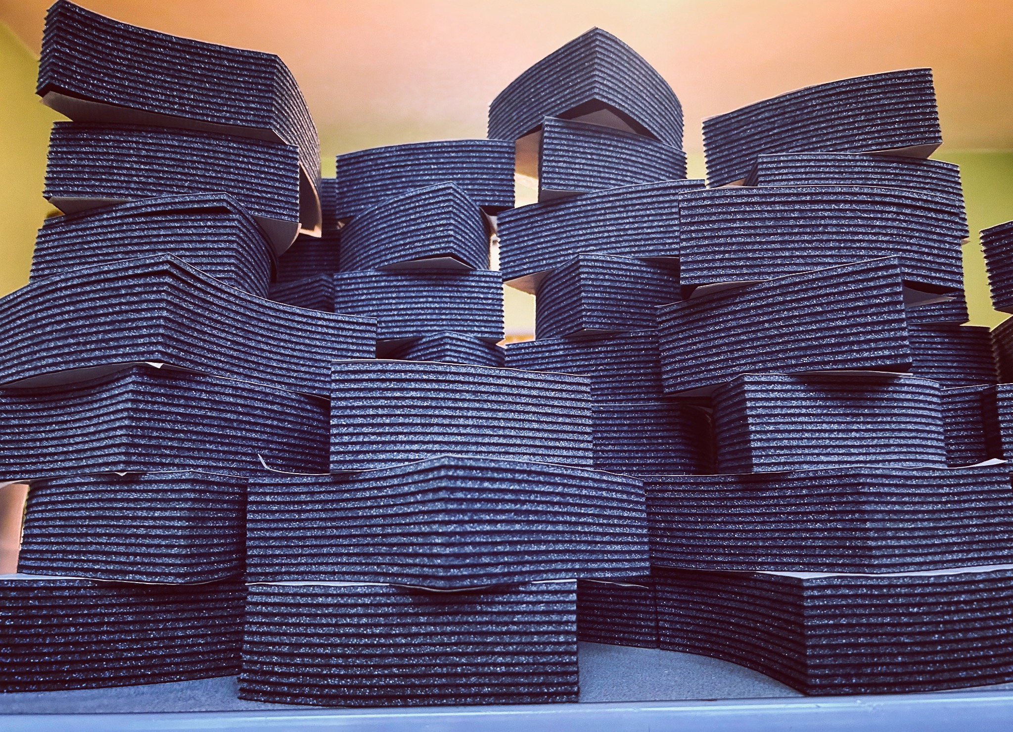 Stos wyciętych, ciemnych elementów z grubej pianki o żłobkowanej strukturze, ułożonych warstwami na sobie. Elementy mają różne kształty, niektóre są zakrzywione.