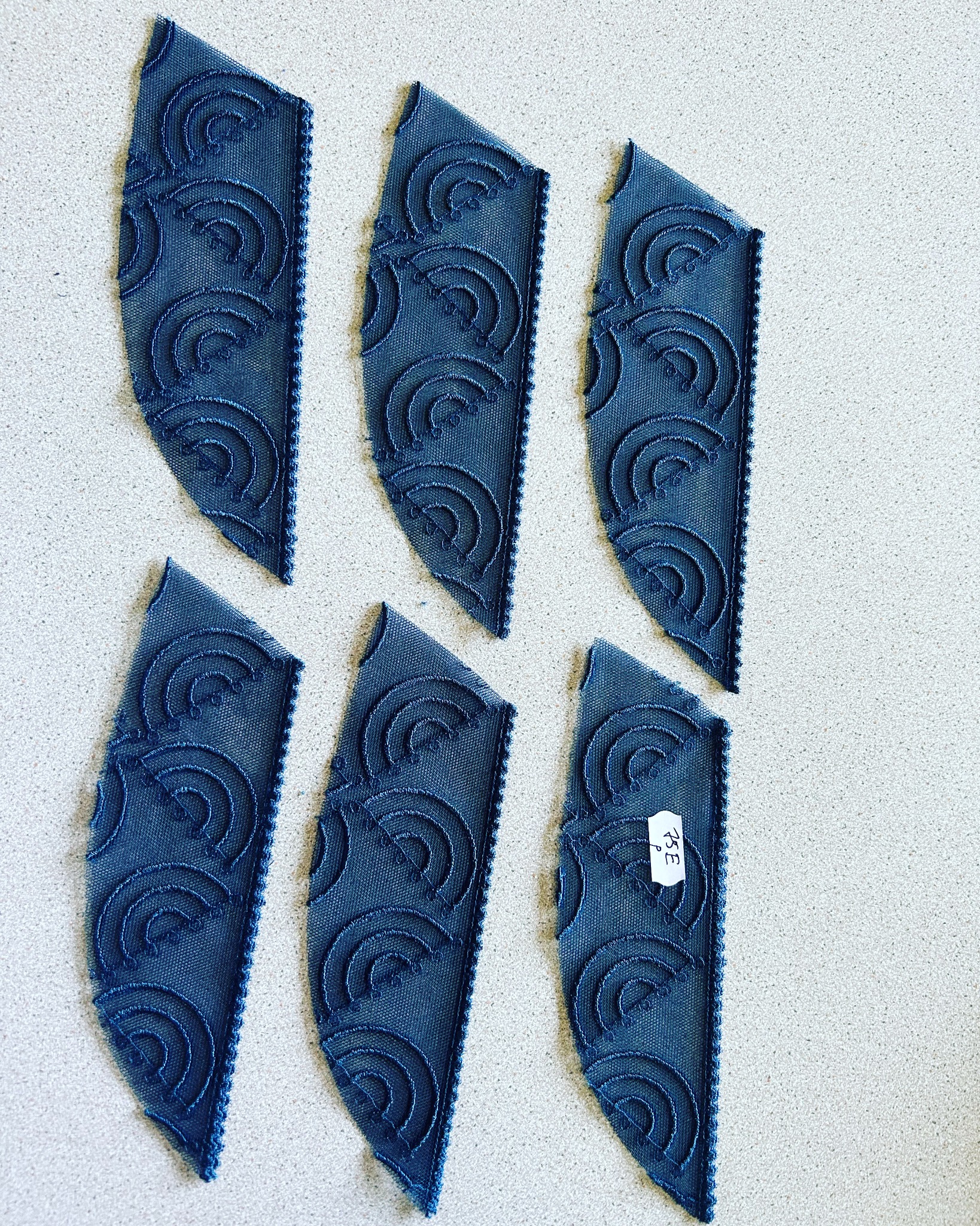 Wykrojone, niebieskie elementy z siateczki z dekoracyjnym wzorem półokręgów, ułożone na jasnym blacie. Jeden element z etykietą.