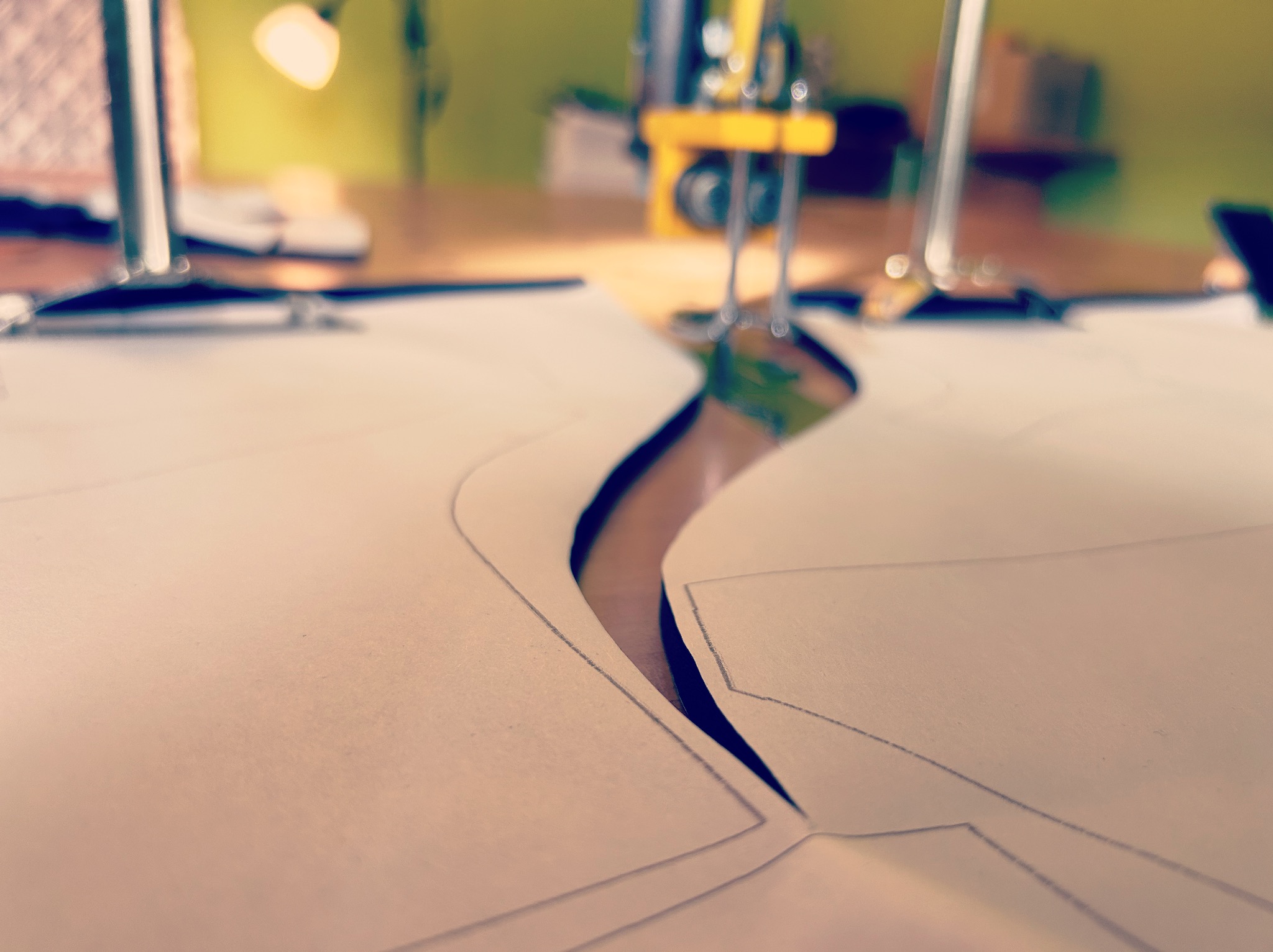 Szablon wykroju odzieży z naniesionymi liniami cięcia, leżący na stole krojczym, z widoczną w tle maszyną do szycia i lampą. Ujęcie z bliska, ciepłe oświetlenie.