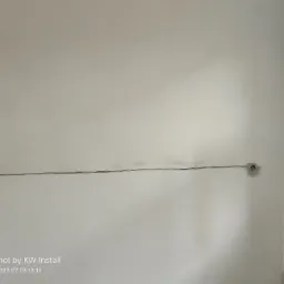 Ściana w trakcie prac elektrycznych: widoczny kabel biegnący wzdłuż ściany i puszka elektryczna z wystającymi przewodami przed montażem gniazdka, obok otwarte okno.