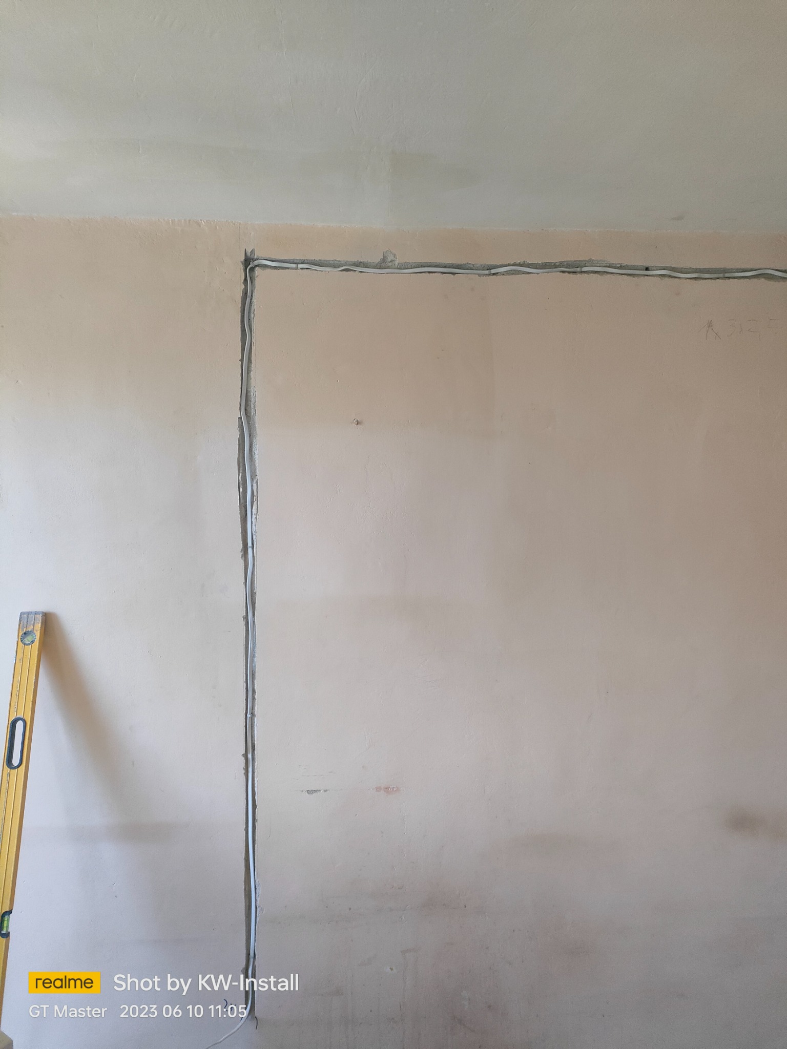 Ściana w trakcie bruzdowania pod przewody elektryczne, widoczna poziomica przy ścianie. Przewody ułożone w wyfrezowanych kanałach.