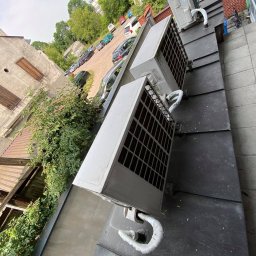 Climatis - Zewnętrzne jednostki klimatyzacji zamontowane na dachu budynku, widok z góry, z widocznymi przewodami i fragmentem parkingu w tle.