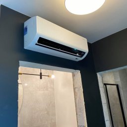 Climatis - Biała jednostka klimatyzacyjna Samsung zamontowana na ciemnoszarej ścianie, widoczny fragment łazienki z szarą glazurą i czarną ramą kabiny prysznicowej, widoczna temperatura 24 stopnie Celsjusza.