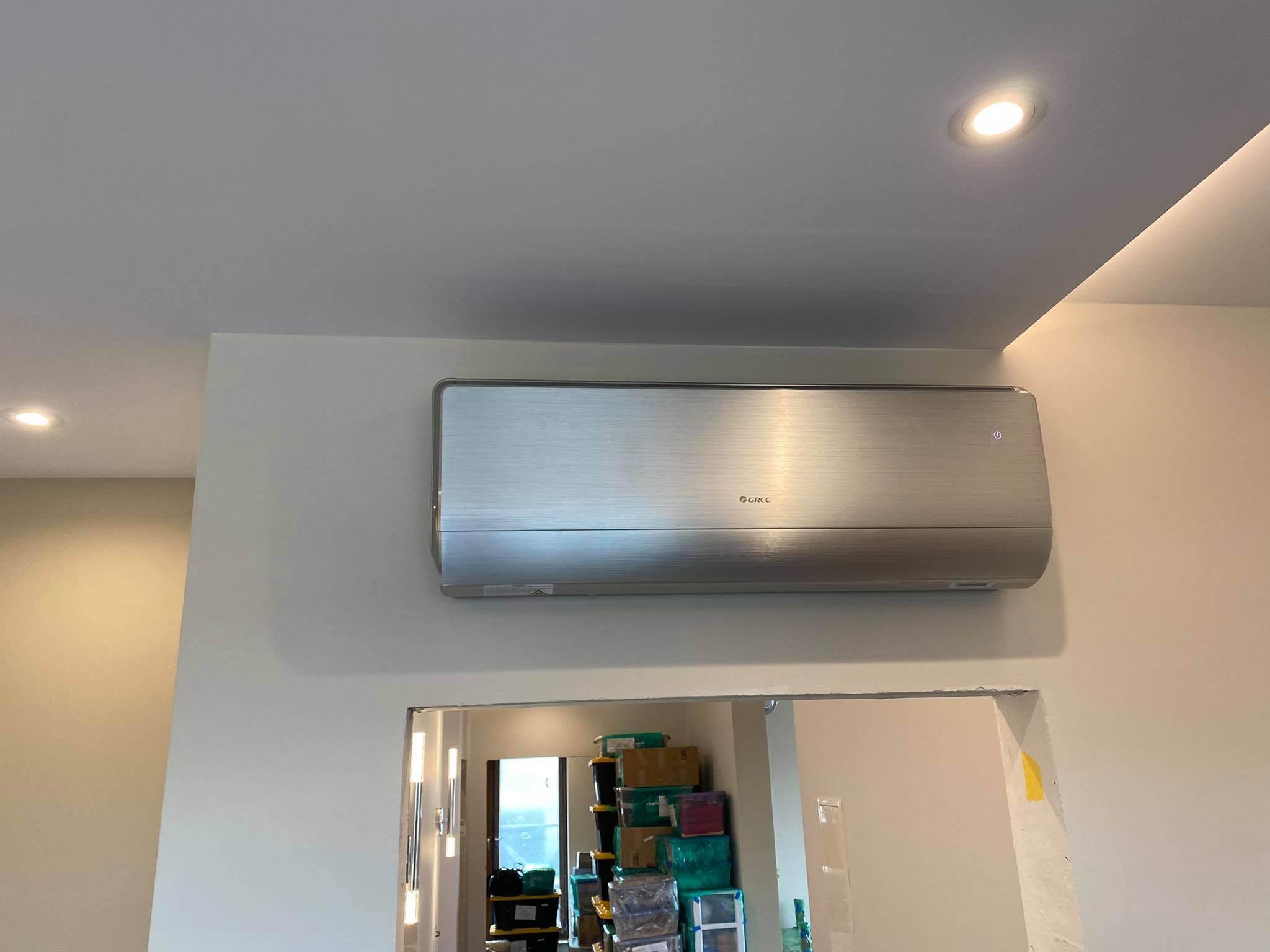 Srebrna jednostka wewnętrzna klimatyzacji marki Gree zamontowana na ścianie w mieszkaniu w Krakowie, widok z dołu, w tle widoczny pokój z kartonami.