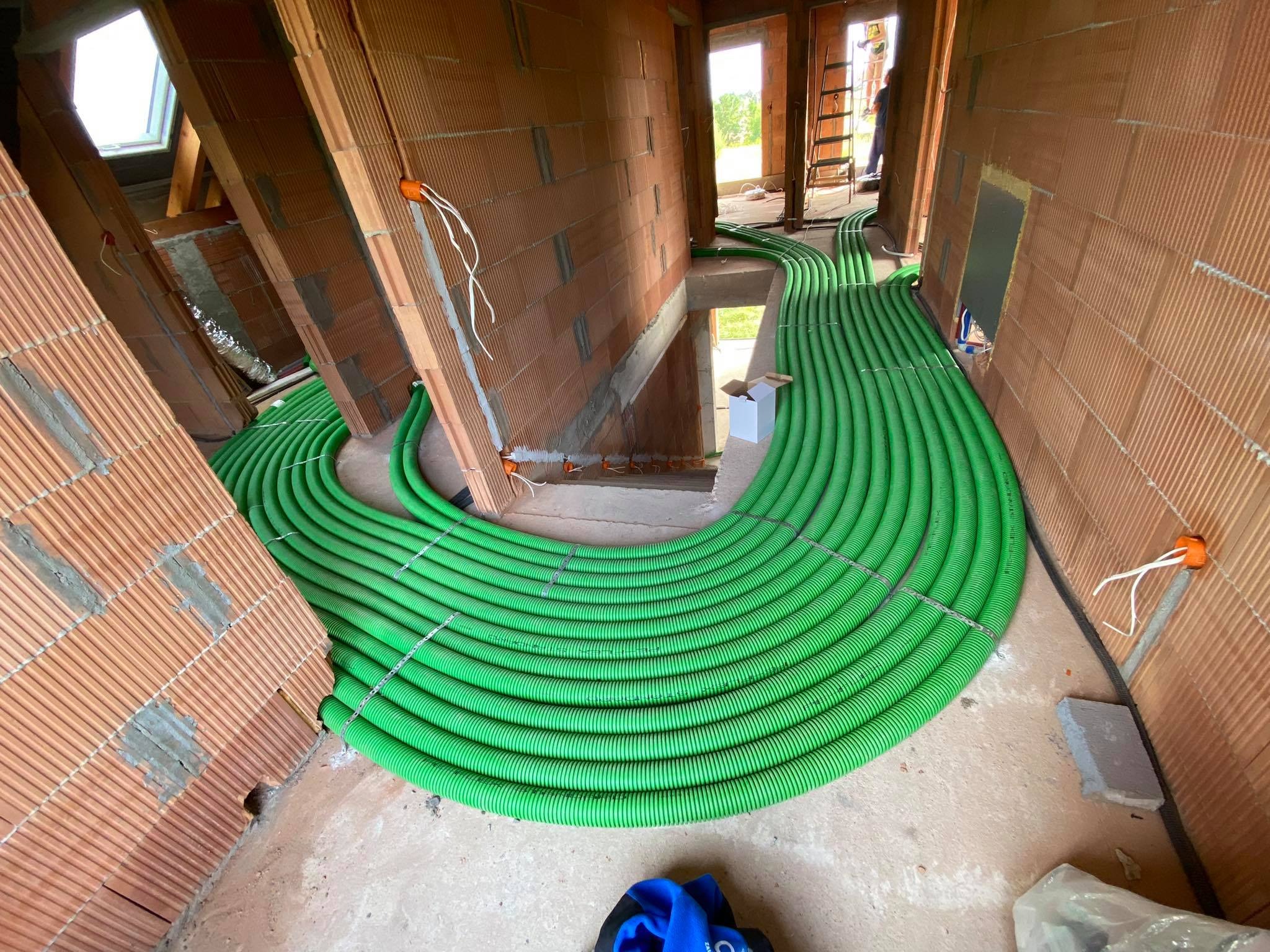 Instalacja rekuperacji: zielone rury wentylacyjne ułożone w pętlę na poddaszu w trakcie montażu, widoczne pomarańczowe puszki elektryczne w ścianach z cegły.