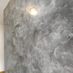 Ściana wewnętrzna pokryta dekoracyjnym tynkiem w odcieniach szarości, z widoczną fakturą i delikatnym połyskiem pod wpływem światła.