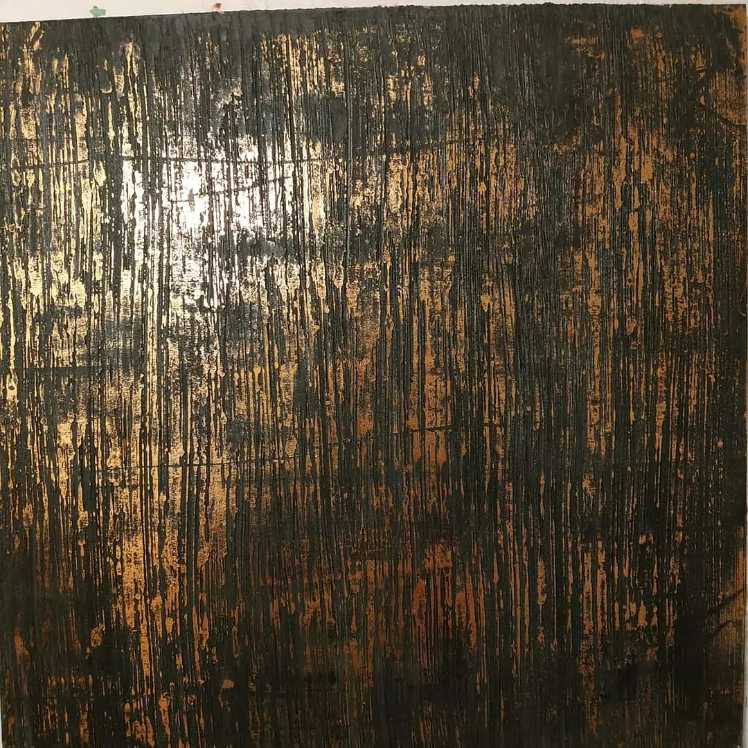 Teksturowana ściana z efektem starego złota, pokryta ciemną farbą z pionowymi smugami, tworząca rustykalny wygląd.