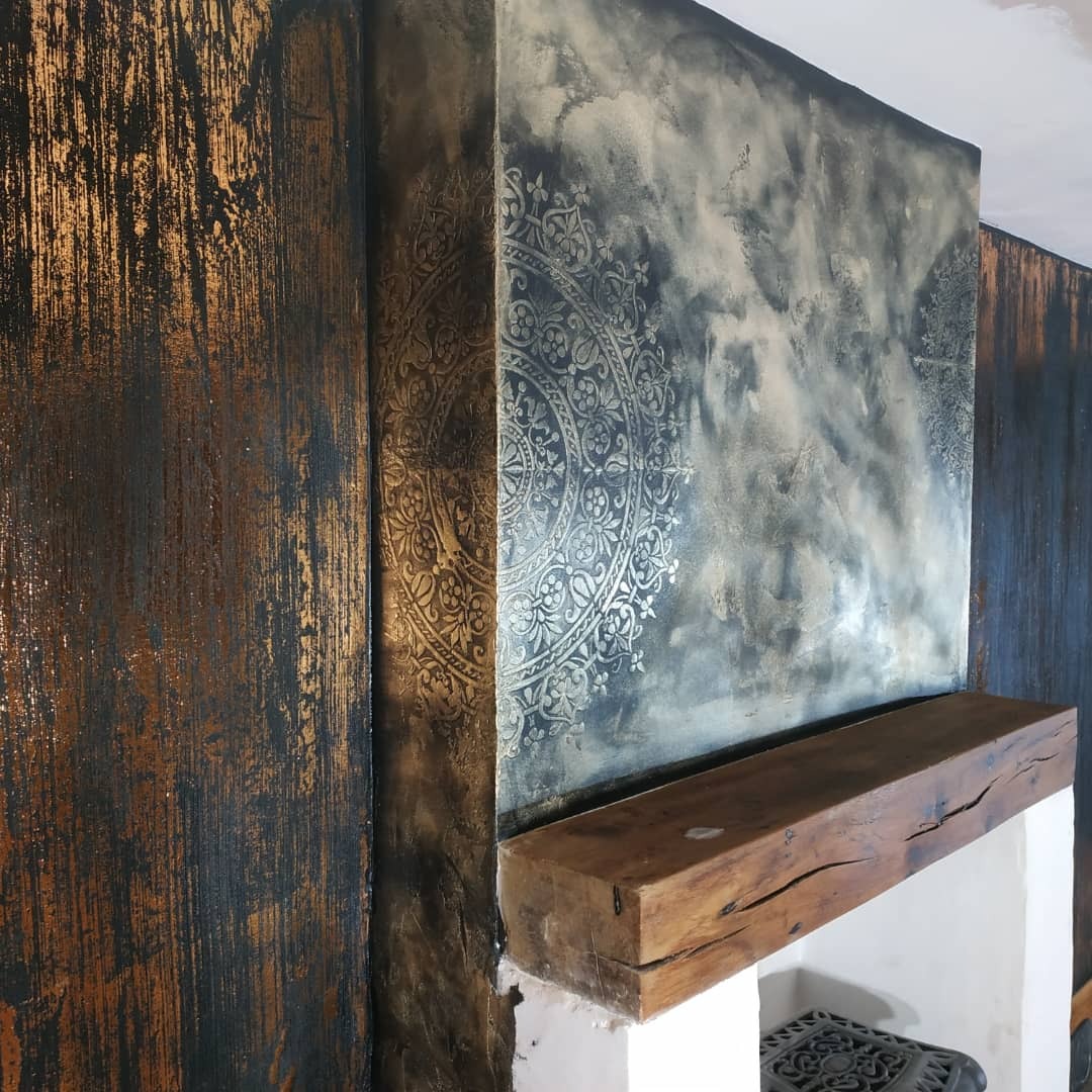 Dekoracyjna ściana z efektem ombre i ornamentem mandali, wykończona drewnianą półką kominkową.