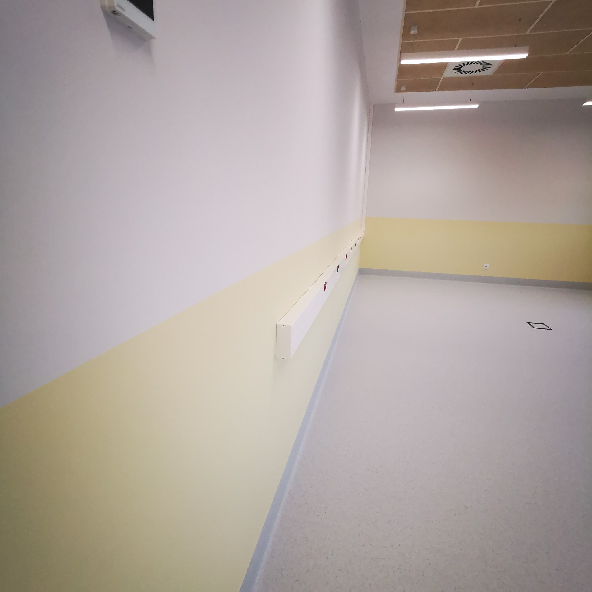 Pomalowane na biało i żółto wnętrze z zamontowanymi listwami przypodłogowymi i osłonami na ścianie, widoczne oświetlenie sufitowe.
