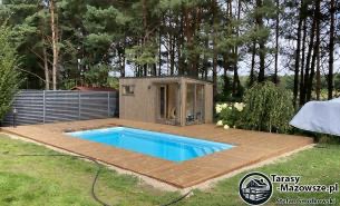 Nowoczesny taras z deski Thermory termo sosna otaczający prostokątny basen, zbudowany na fundamentach punktowych z konstrukcją krzyżową samonośną, w tle domek ogrodowy i zielony trawnik.