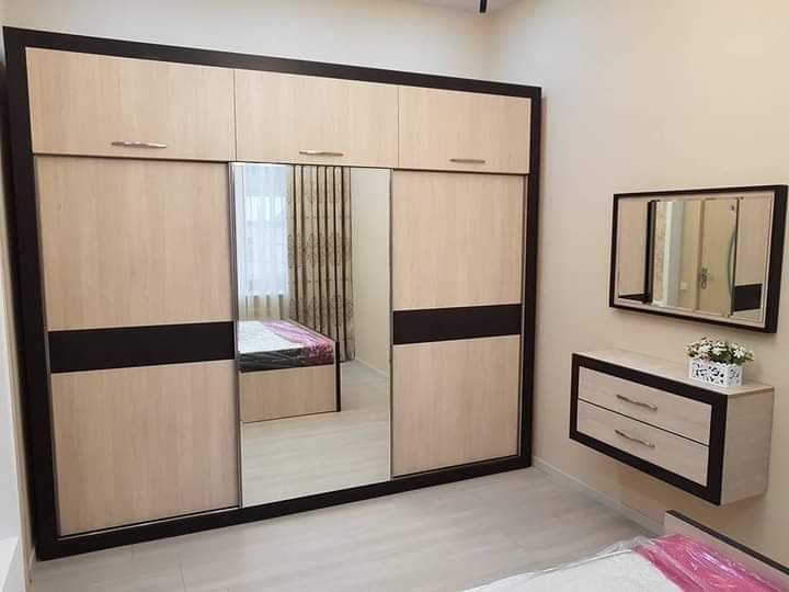 Duża szafa przesuwna z lustrami i nadstawką w kolorze jasnego drewna z ciemnobrązowymi akcentami, uzupełniona wiszącą komodą z lustrem i kwiatami w doniczce.