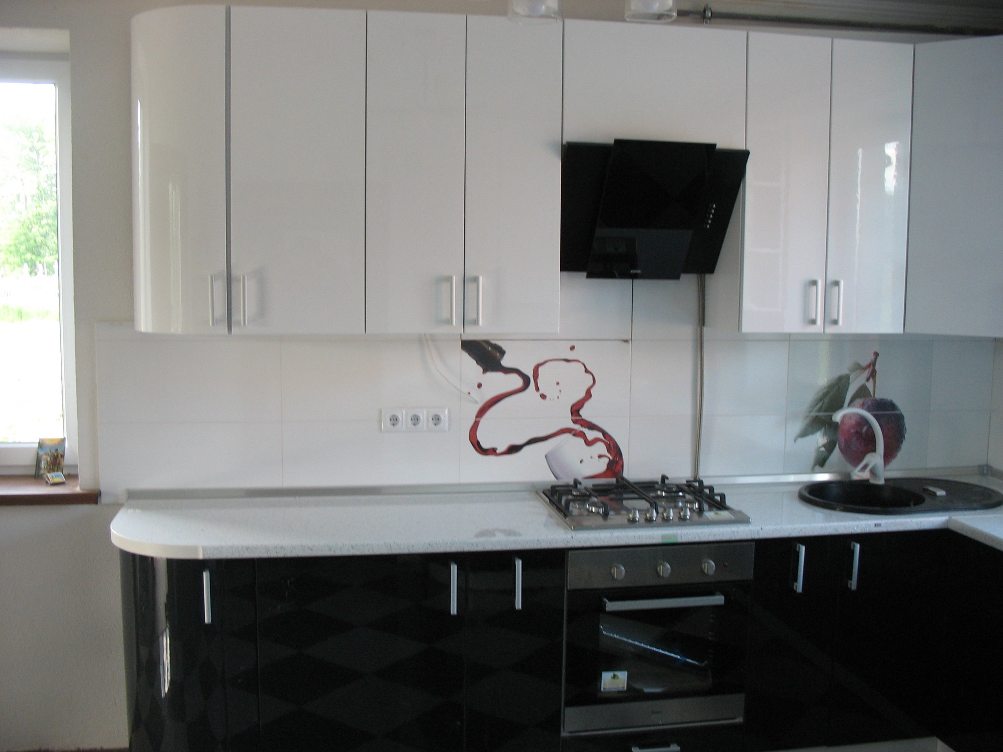 Nowoczesna kuchnia z białymi szafkami górnymi i czarnymi dolnymi, wzór na ścianie imitujący rozlane wino, czarny okap, płyta gazowa.