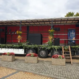 Scena mobilna na przyczepie ciężarówki, udekorowana kukurydzą i kwiatami w donicach, z nagłośnieniem i oświetleniem oraz banerem DJ-a