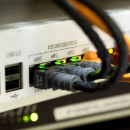 Szczegółowe zbliżenie na porty Ethernet routera z podłączonymi kablami sieciowymi; aktywne połączenia sygnalizowane zielonymi diodami LED.