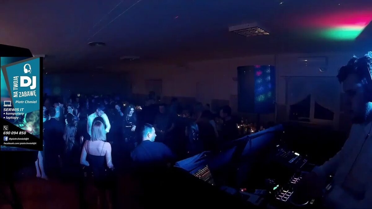 DJ grający muzykę na imprezie, widoczny tłum tańczących osób, oświetlenie dyskotekowe i baner reklamowy z ofertą usług IT.