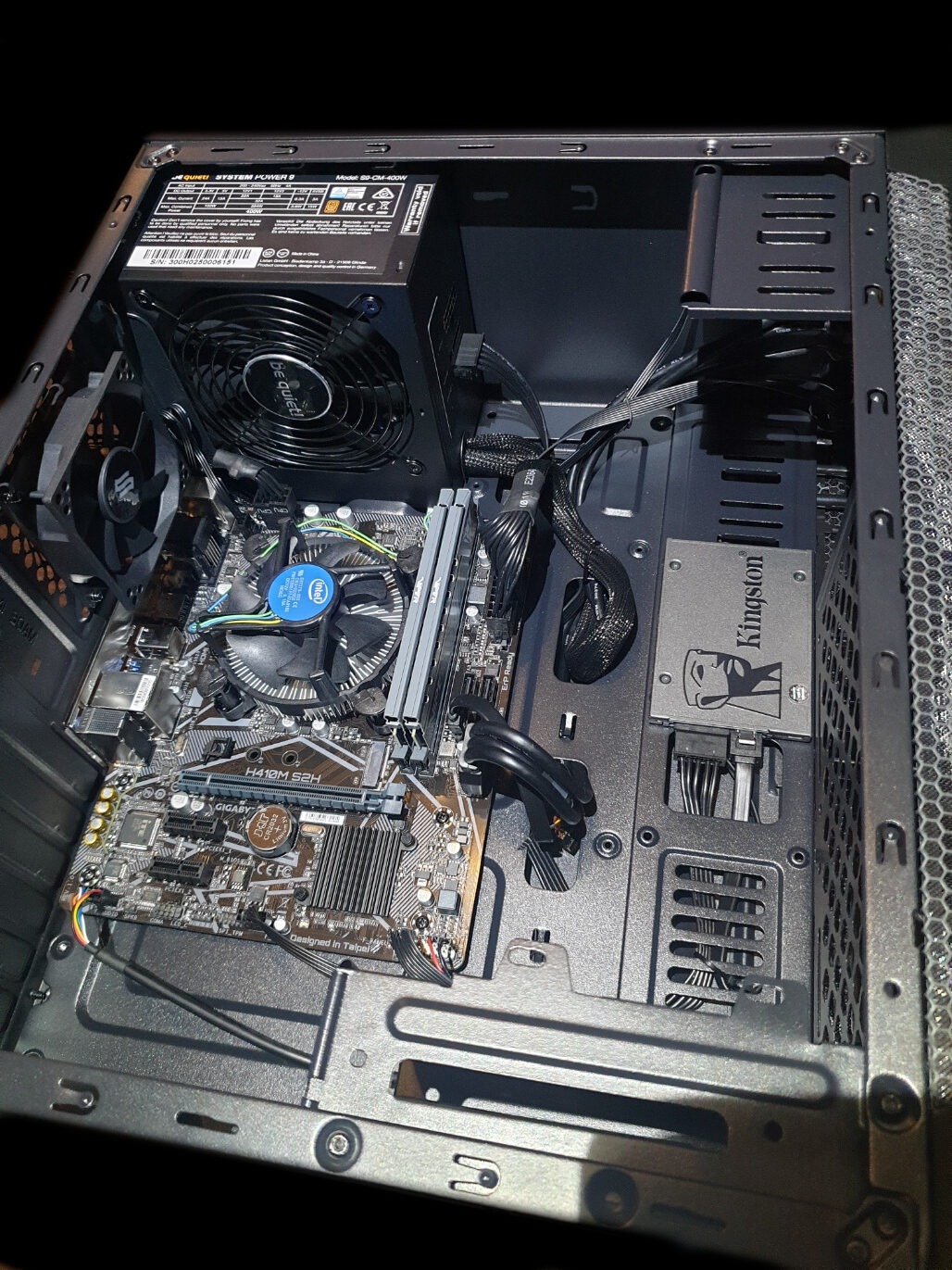 Wnętrze obudowy komputera stacjonarnego z widoczną płytą główną Gigabyte H410M S2H, procesorem Intel z chłodzeniem, pamięcią RAM, zasilaczem Be Quiet System Power 9 400W i dyskiem SSD Kingston...