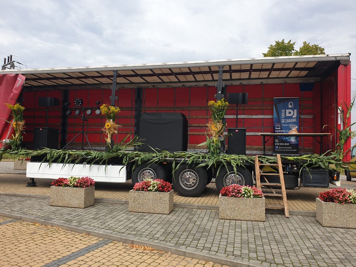Scena mobilna na przyczepie ciężarówki, udekorowana kukurydzą i kwiatami w donicach, z nagłośnieniem i oświetleniem oraz banerem DJ-a