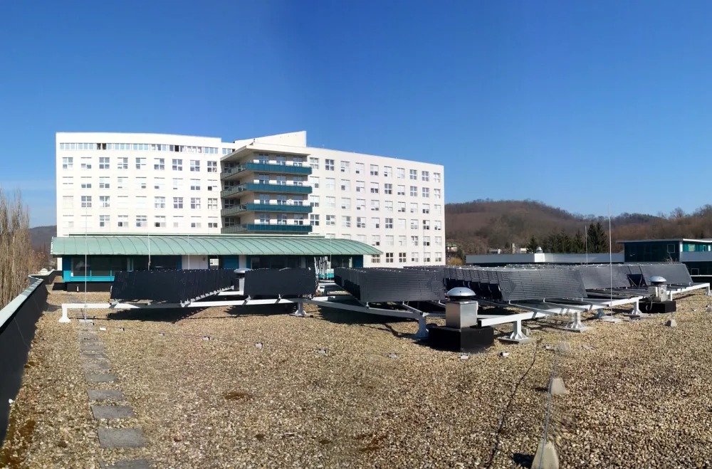 Rząd kolektorów słonecznych na płaskim dachu budynku szpitalnego w słoneczny dzień.