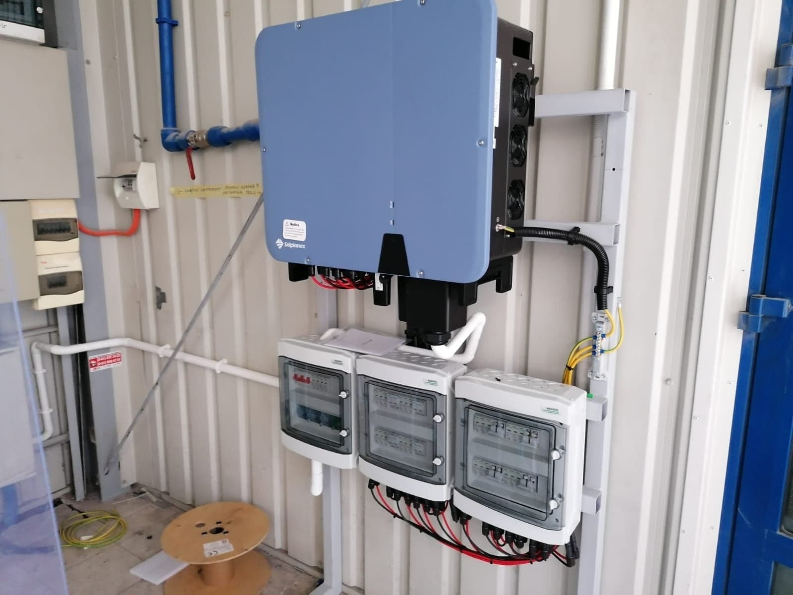 Zamontowany falownik z trzema rozdzielnicami na metalowej konstrukcji w pomieszczeniu technicznym, widoczne okablowanie i elementy instalacji.