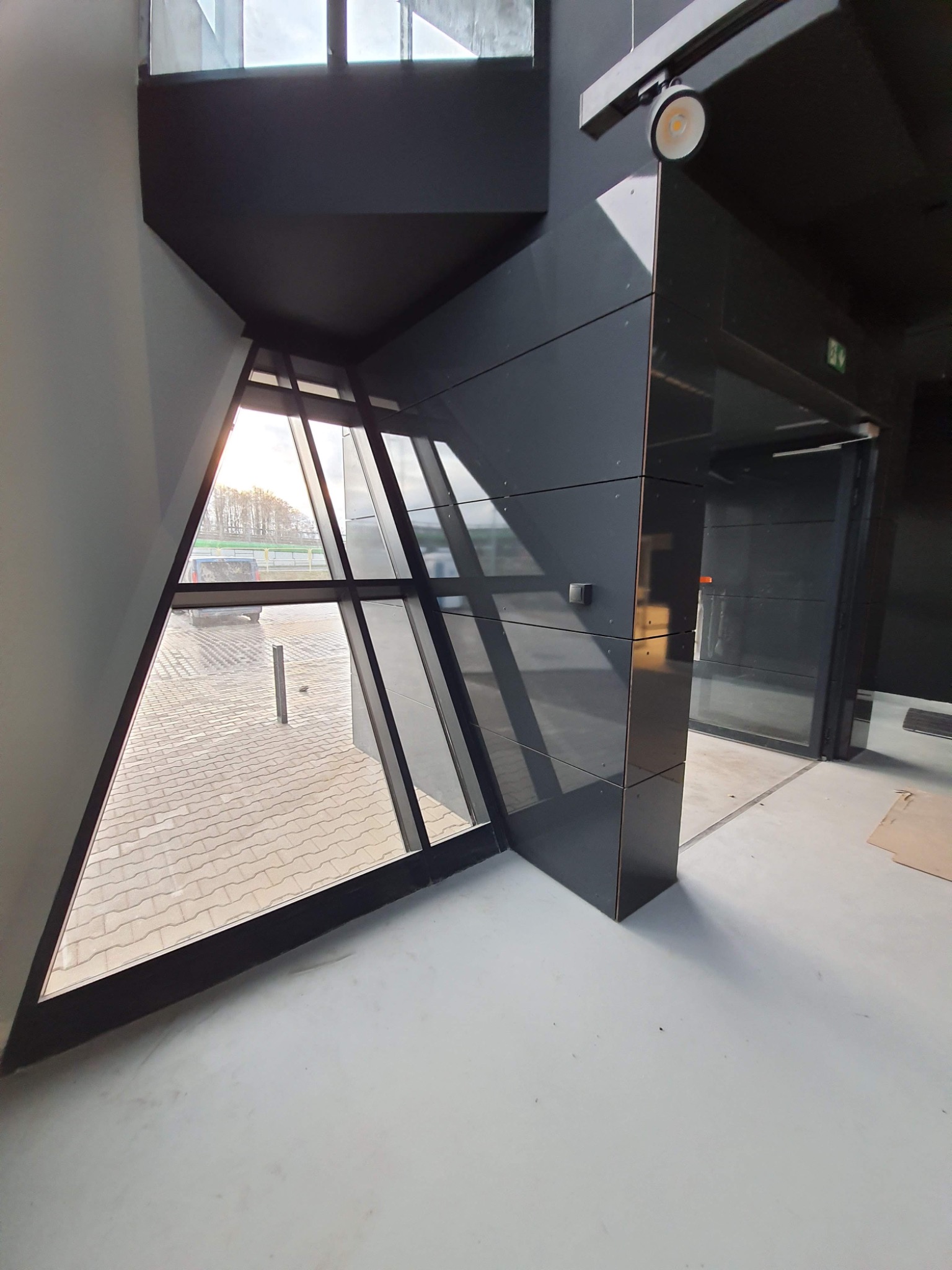 Nowoczesne, czarno-białe wnętrze biura w Poznaniu z geometrycznym oknem i widokiem na zewnątrz, świeżo wykończona podłoga.