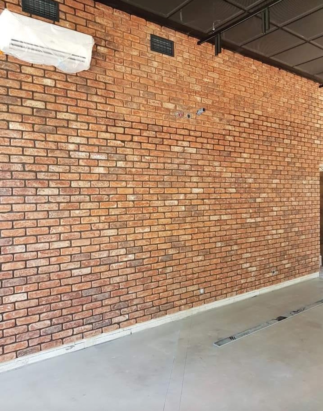 Ściana z cegły klinkierowej w biurze z klimatyzacją, widoczne instalacje elektryczne i wentylacja pod sufitem.