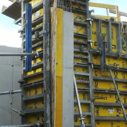 Szczegółowe ujęcie szalunku Doka z żółtymi panelami, metalowymi elementami konstrukcyjnymi i świeżym betonem, uchwycone z bliska na tle częściowo widocznego nieba.