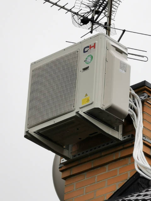 Zewnętrzna jednostka klimatyzacji marki CH zamontowana na ceglanym kominie w Bielsku-Białej, widoczne kable i antena telewizyjna na dachu.