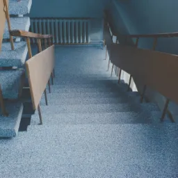 Schody w budynku wykończone jasnoniebieską posadzką z drobnymi, ciemniejszymi elementami, widoczne metalowe barierki, ujęcie z góry.