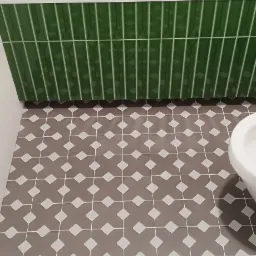 Łazienka z wanną obłożoną pionowymi, zielonymi płytkami oraz podłogą z szarych płytek w geometryczny wzór z białymi rombami.