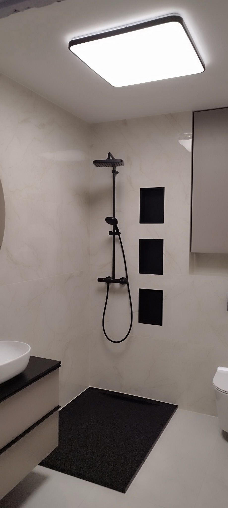 Nowoczesna łazienka z czarnym zestawem prysznicowym, trzema wnękami w ścianie, umywalką nablatową i czarnym brodzikiem bez kabiny.