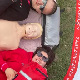 Instruktorzy pierwszej pomocy z manekinem do resuscytacji i torbą medyczną leżący na trawie podczas przerwy w szkoleniu.