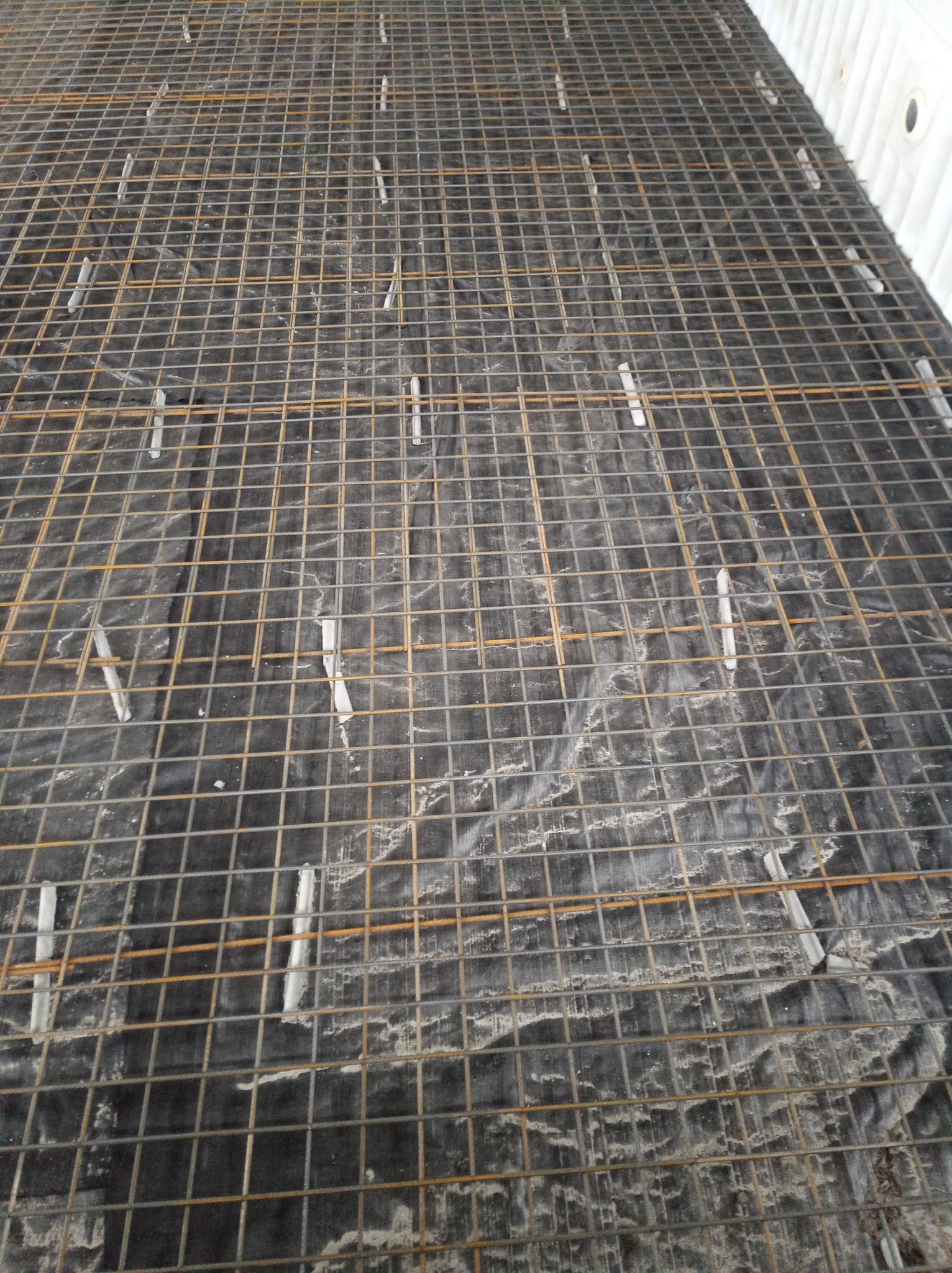 Siatka zbrojeniowa ułożona na czarnej folii z dystansami z tworzywa sztucznego, przygotowana do wylania betonu.