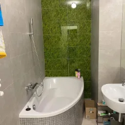 Nowoczesna łazienka z wanną narożną obudowaną mozaiką, umywalką nablatową i ścianą z zielonego mchu.