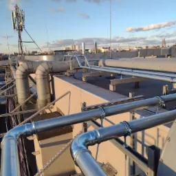 System rur wentylacyjnych na dachu budynku w Kielcach, widoczne złącza i mocowania, w tle panorama miasta pod błękitnym niebem.