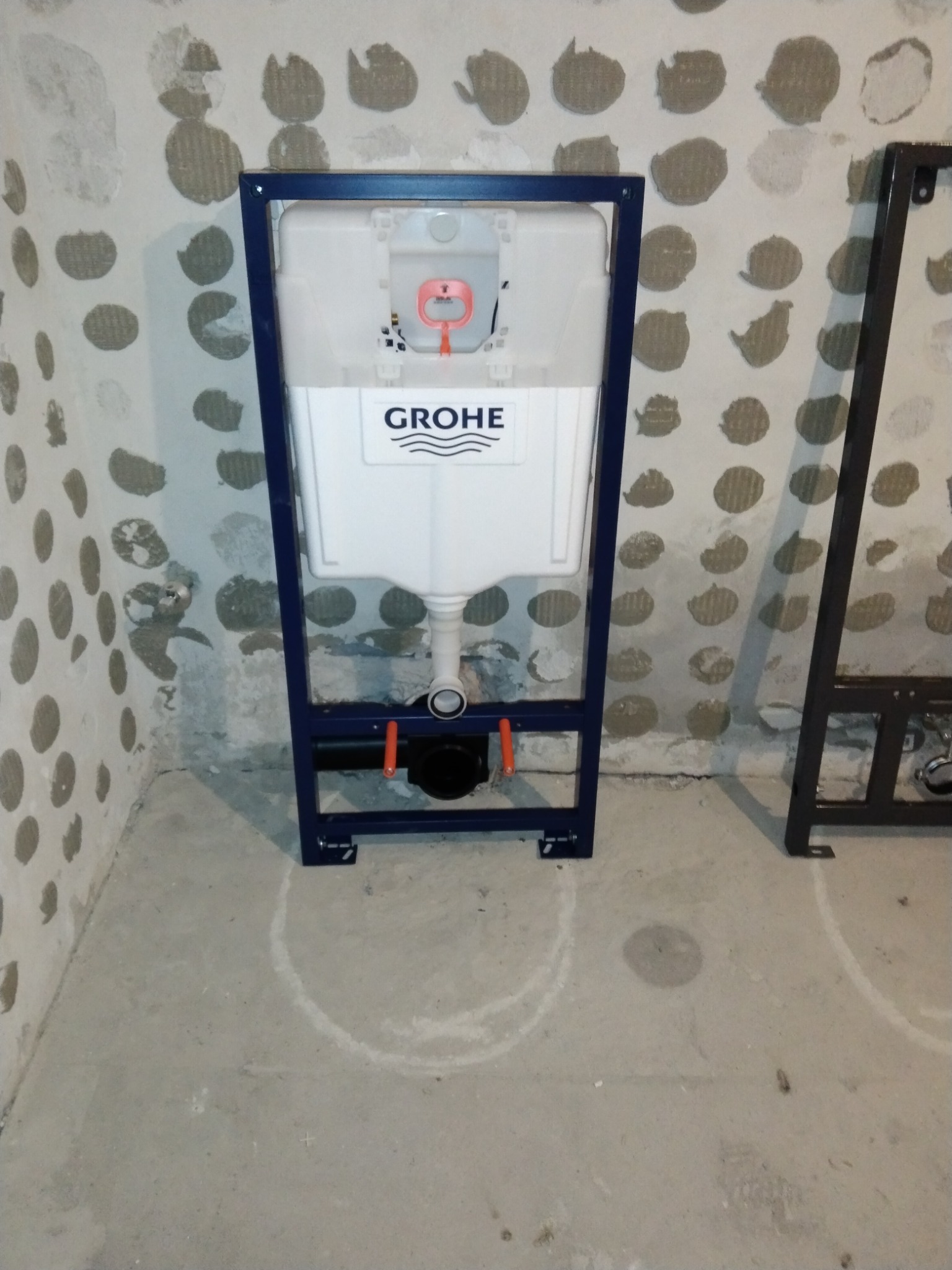 Stelaż podtynkowy Grohe zamontowany w surowym pomieszczeniu z widocznymi śladami po wierceniu na ścianie i podłodze, przygotowany do dalszych prac wykończeniowych.