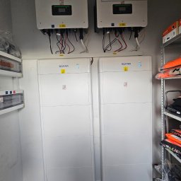 MK SUN Mateusz Karbowiak - Dwa białe inwertery i dwa magazyny energii SOFAR zamontowane w pomieszczeniu. Widoczne kable i instalacja elektryczna. Półka z ubraniami w tle.