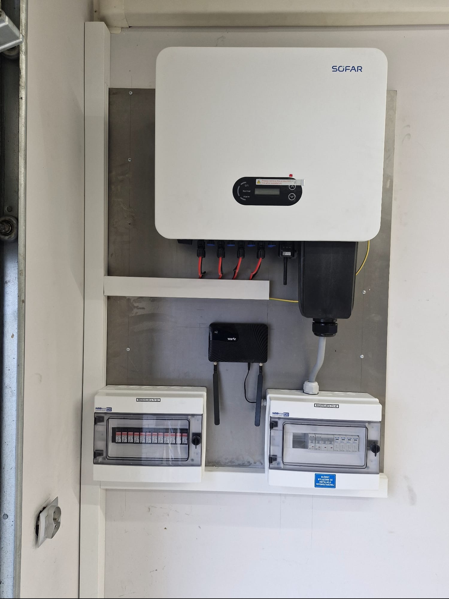 Kompletna instalacja fotowoltaiczna wewnątrz pomieszczenia: inwerter Sofar, rozdzielnice AC/DC, router Zyxel. Widoczne okablowanie i zabezpieczenia.