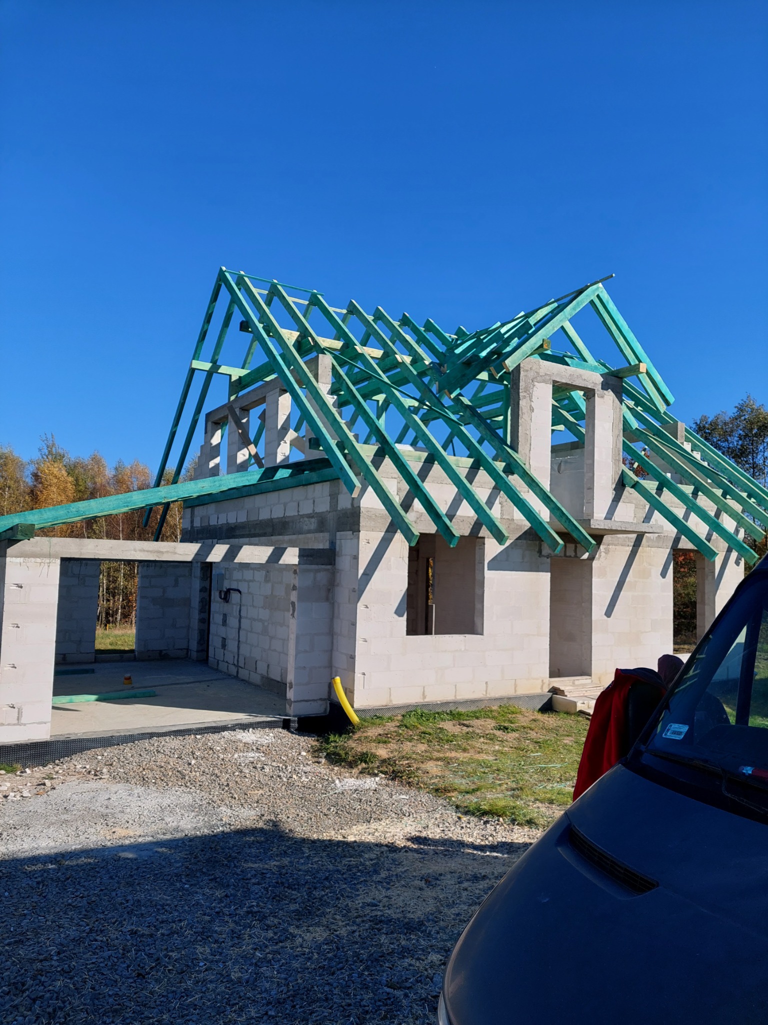 Budowa domu jednorodzinnego w Wiśniowej na etapie montażu drewnianej konstrukcji dachu, widok na niezadaszony budynek z szarą elewacją z betonu komórkowego i zieloną impregnacją więźby dachowej,...