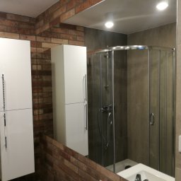 MM Perfekt Maciej Majewski - Nowoczesna łazienka z prysznicem w kabinie z przesuwanymi drzwiami, umywalką wpuszczaną w blat, białymi szafkami wiszącymi z długimi uchwytami i ścianą wyłożoną cegłą.