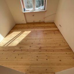 Project MasterWood Przemysław Bejmert - Jasna, drewniana podłoga po renowacji w pokoju na poddaszu, widok z góry. Świeże drewno oświetlone słońcem, Warszawa.