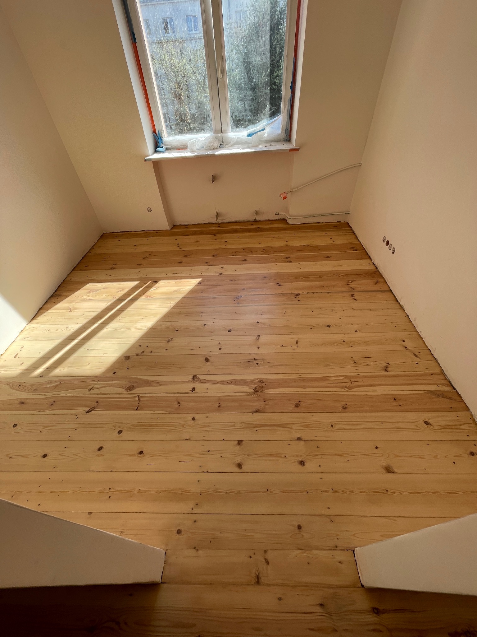 Jasna, drewniana podłoga po renowacji w pokoju na poddaszu, widok z góry. Świeże drewno oświetlone słońcem, Warszawa.