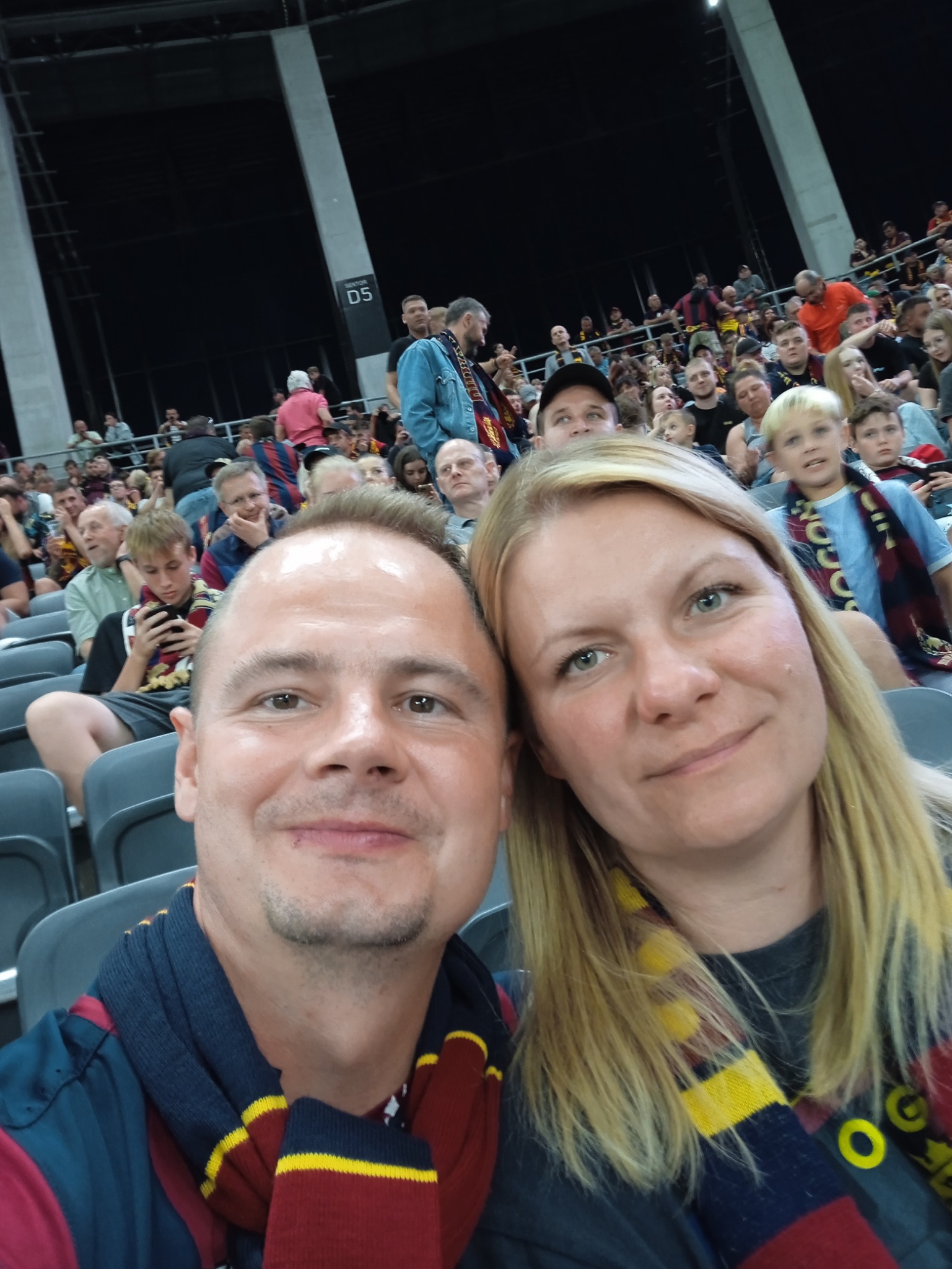 Para kibiców w szalikach w barwach klubowych robi selfie na trybunach stadionu podczas meczu.