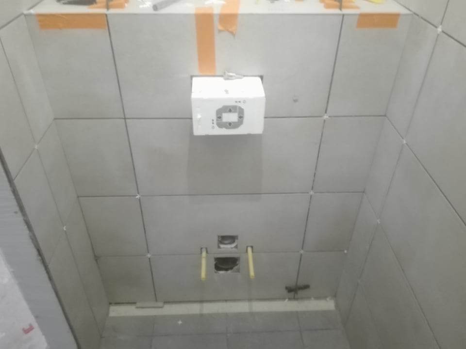 Świeżo ułożone, jasnoszare płytki w łazience, z widocznymi krzyżykami dystansowymi i taśmą malarską, przygotowane do fugowania, z zamontowanym stelażem podtynkowym WC.