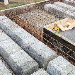 Wieniec stropowy z szalunkiem traconym z betonu komórkowego, zbrojony stalą, widok z góry na tle budynków mieszkalnych i drzew