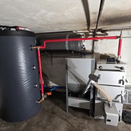 SUNUPS DANIEL ŻESŁAWSKI - Zestaw kotła na pellet z zasobnikiem i zbiornikiem buforowym w kotłowni. Widoczne rury w izolacji termicznej. Instalacja grzewcza w piwnicy.