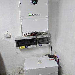SUNUPS DANIEL ŻESŁAWSKI - Biały inwerter Growatt z rozdzielnicami PV-DC i PV-AC oraz modułowy magazyn energii w pomieszczeniu. Widoczne okablowanie i elementy instalacji.