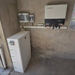 SUNUPS DANIEL ŻESŁAWSKI - Instalacja magazynu energii Growatt w garażu w Seceminie. Widoczne liczniki, inwerter i moduły bateryjne. Szara ściana i betonowa podłoga. Widok z boku.