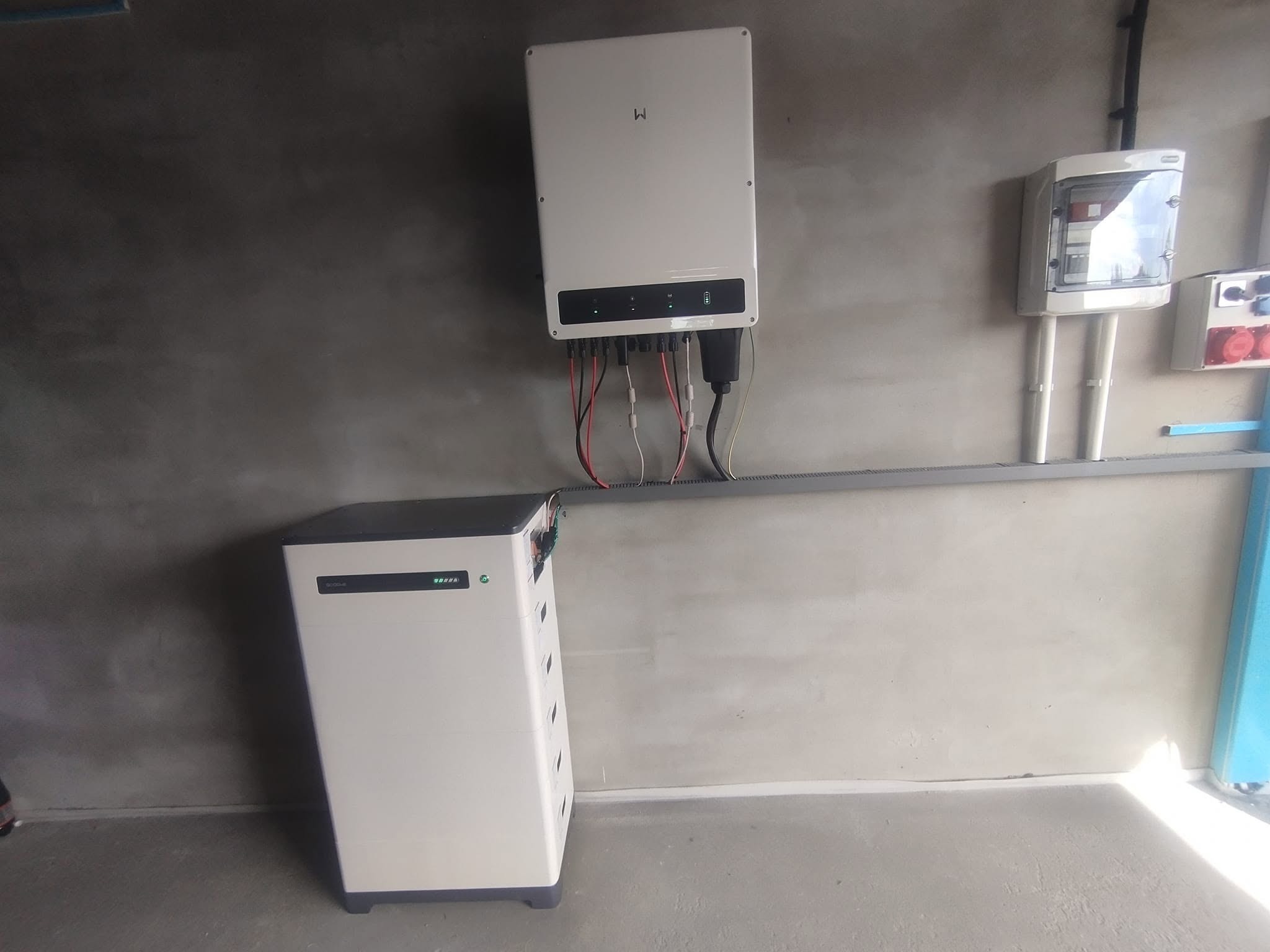 Instalacja magazynu energii i inwertera w Secemin. Biała obudowa magazynu z diodami LED, szary inwerter na ścianie, okablowanie. Nowoczesne rozwiązanie dla domu.