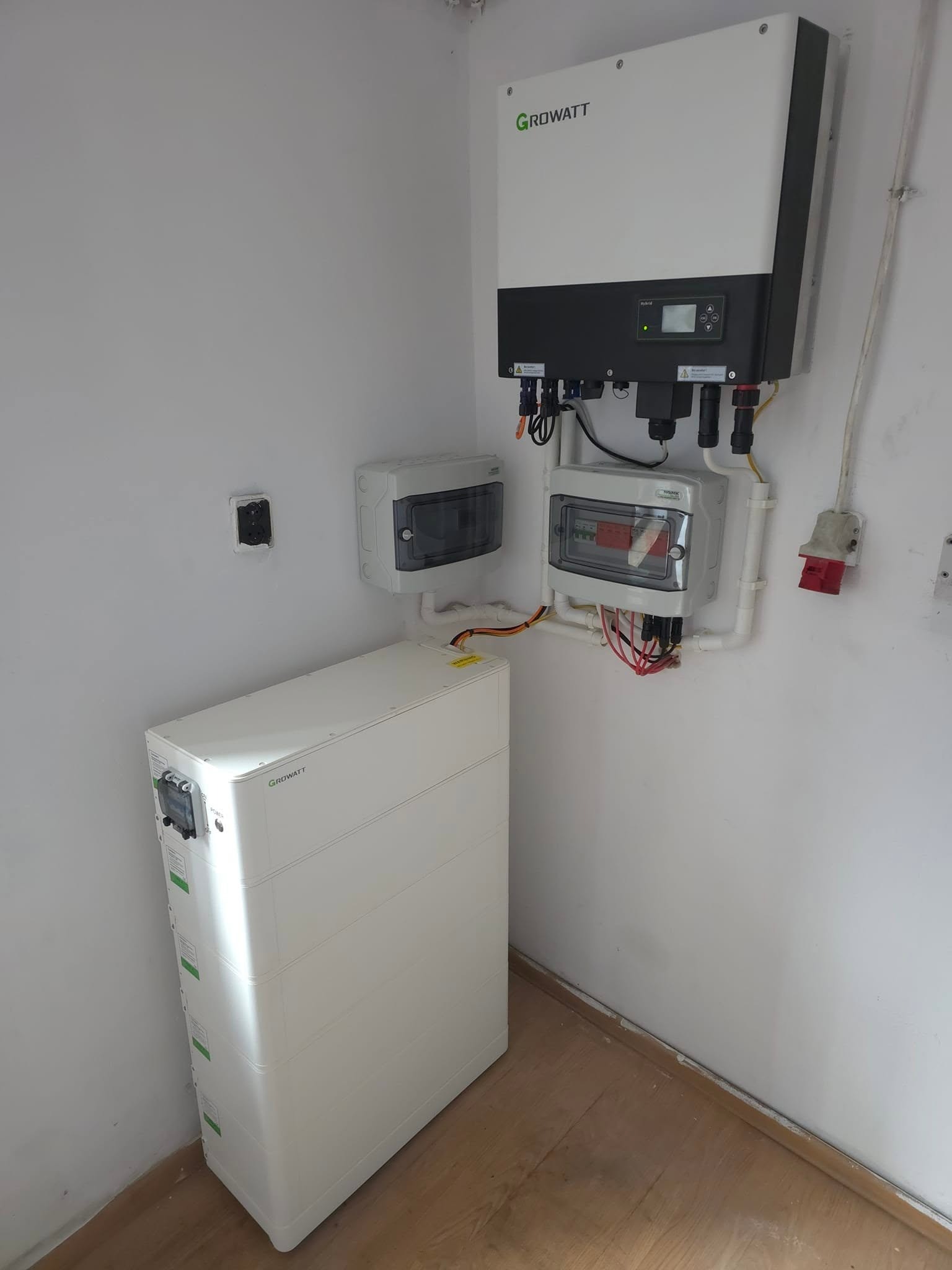 Biały magazyn energii Growatt, inwerter i rozdzielnice na ścianie w pomieszczeniu. Widoczne kable i instalacja elektryczna. Ujęcie z dołu, z perspektywy podłogi.