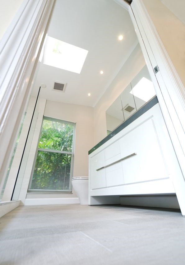 Nowoczesna, jasna łazienka z oknem i roletami, białą szafką z umywalką oraz podwieszaną toaletą, widziana z niskiej perspektywy.